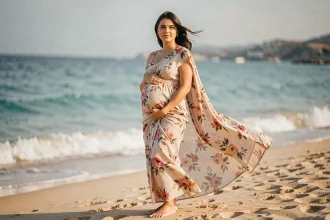 Femme enceinte portant un paréo robe fleuri sur une plage de sable fin avec mer turquoise en fond